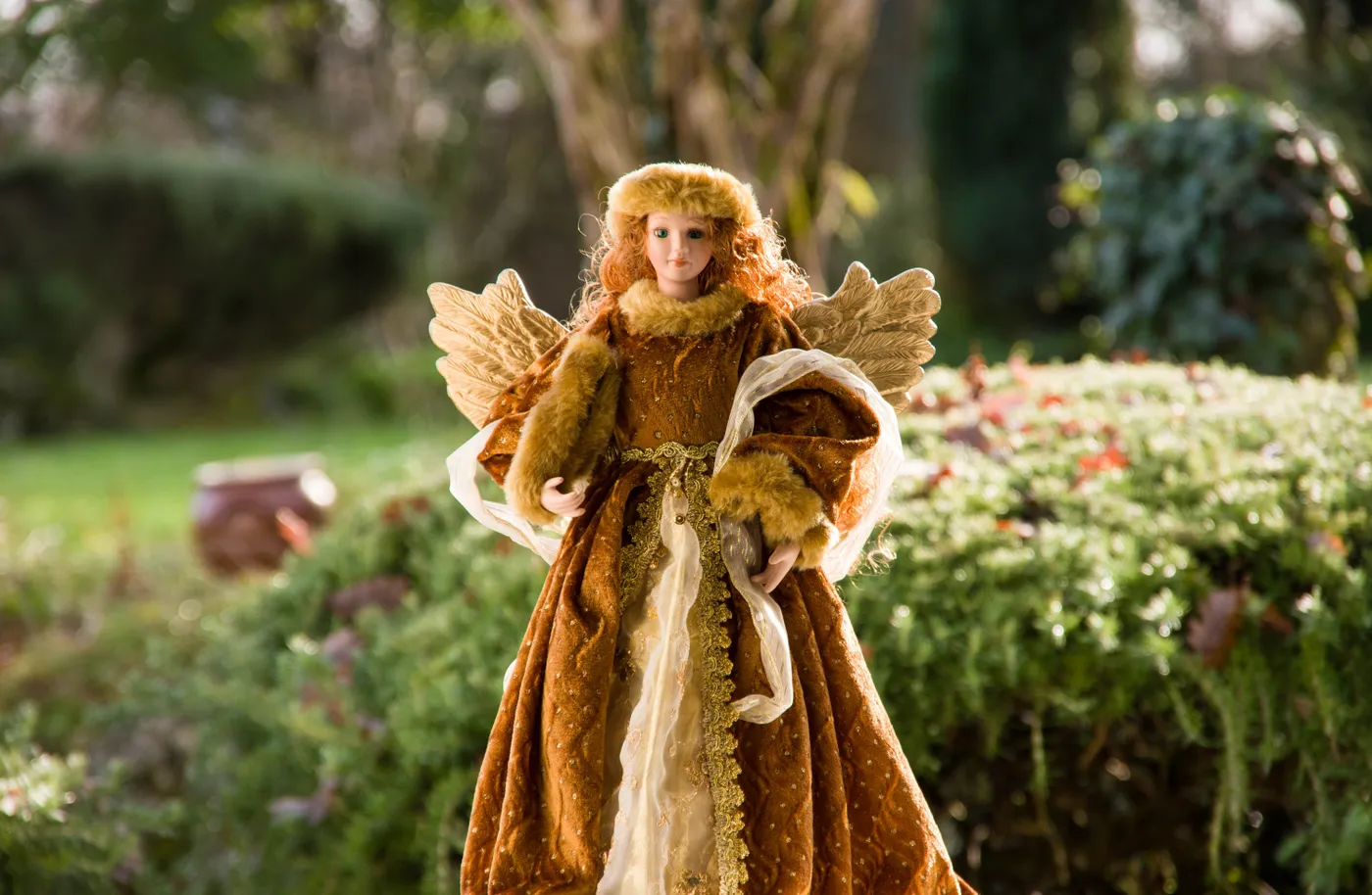 A beautifully crafted angel figurine with wings in a vibrant garden setting.