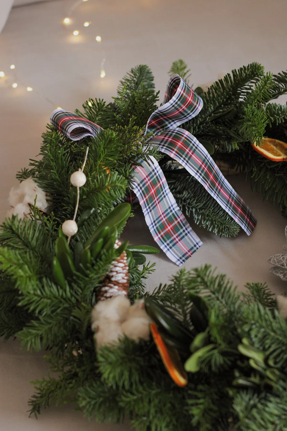A beautifully decorated Christmas wreath featuring a plaid ribbon and natural elements like pine and cotton.