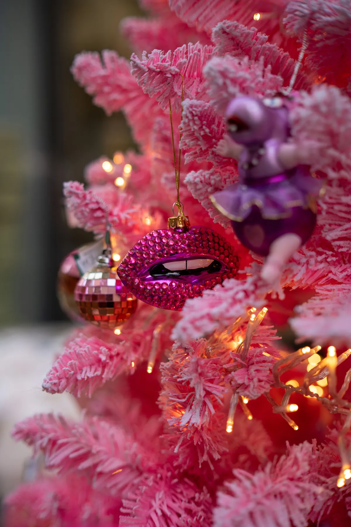 A dazzling pink Christmas tree adorned with unique ornaments shines brightly indoors.