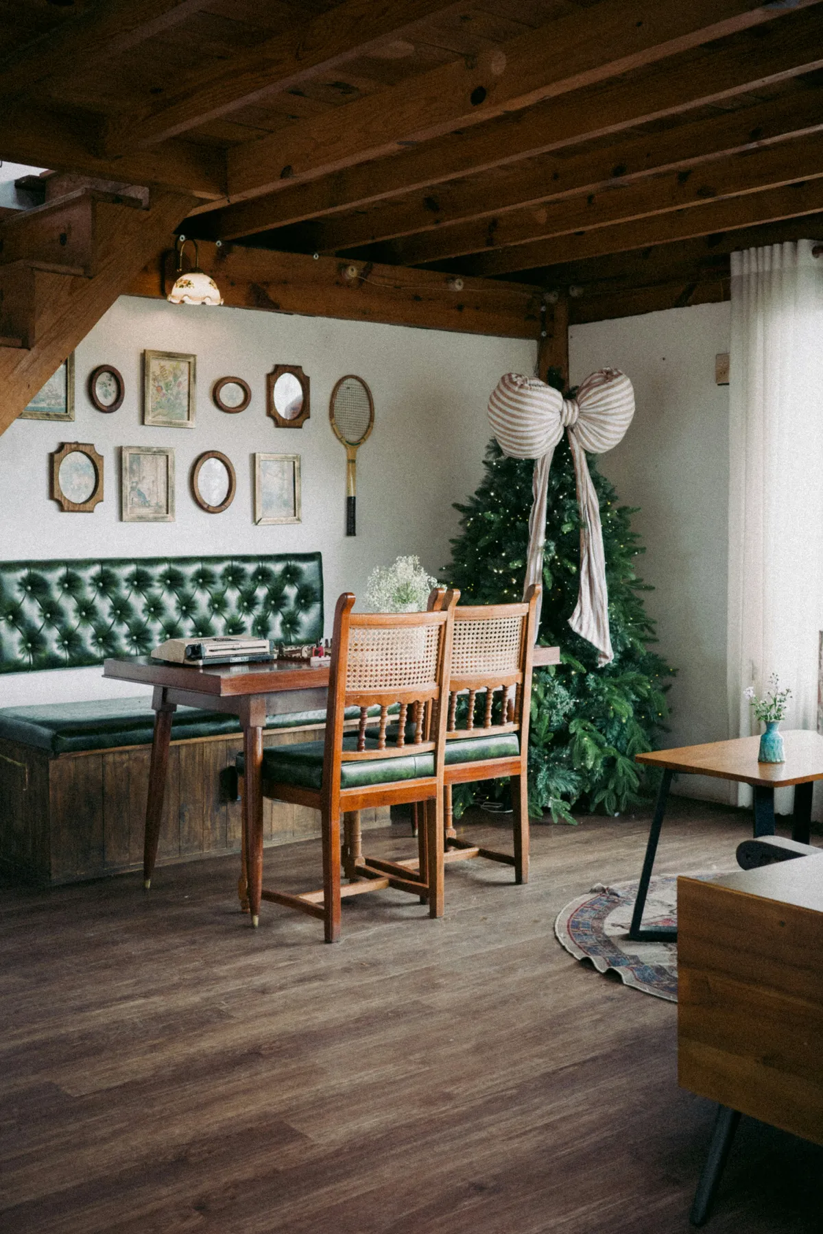 A dining area with a green tufted bench and wooden chairs near a Christmas tree