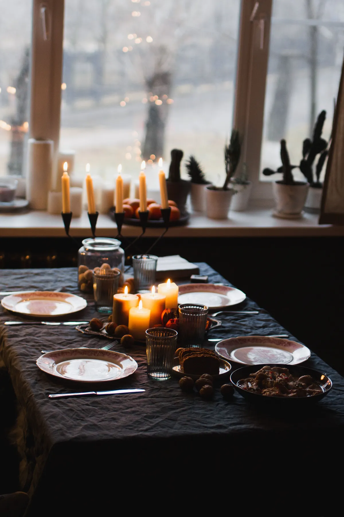 A warm, candlelit table set for dinner, creating a cozy atmosphere indoors beside a winter window.