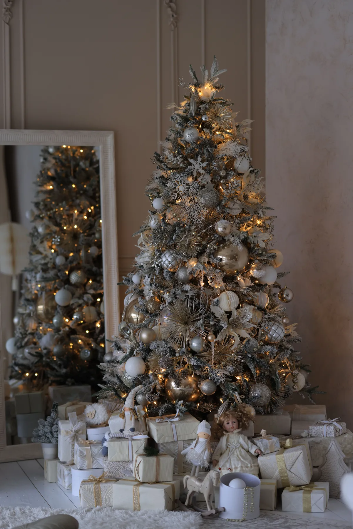 Beautifully decorated Christmas tree with silver ornaments and gifts in a cozy setting.