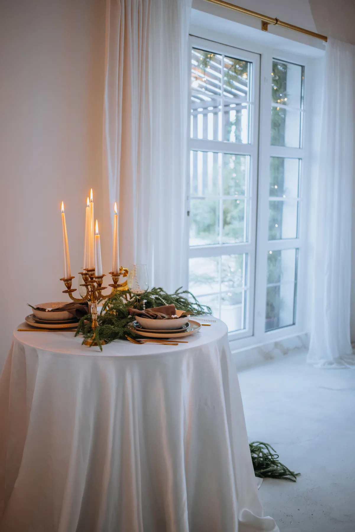 Candle-lit holiday table setting by the window with festive decor.