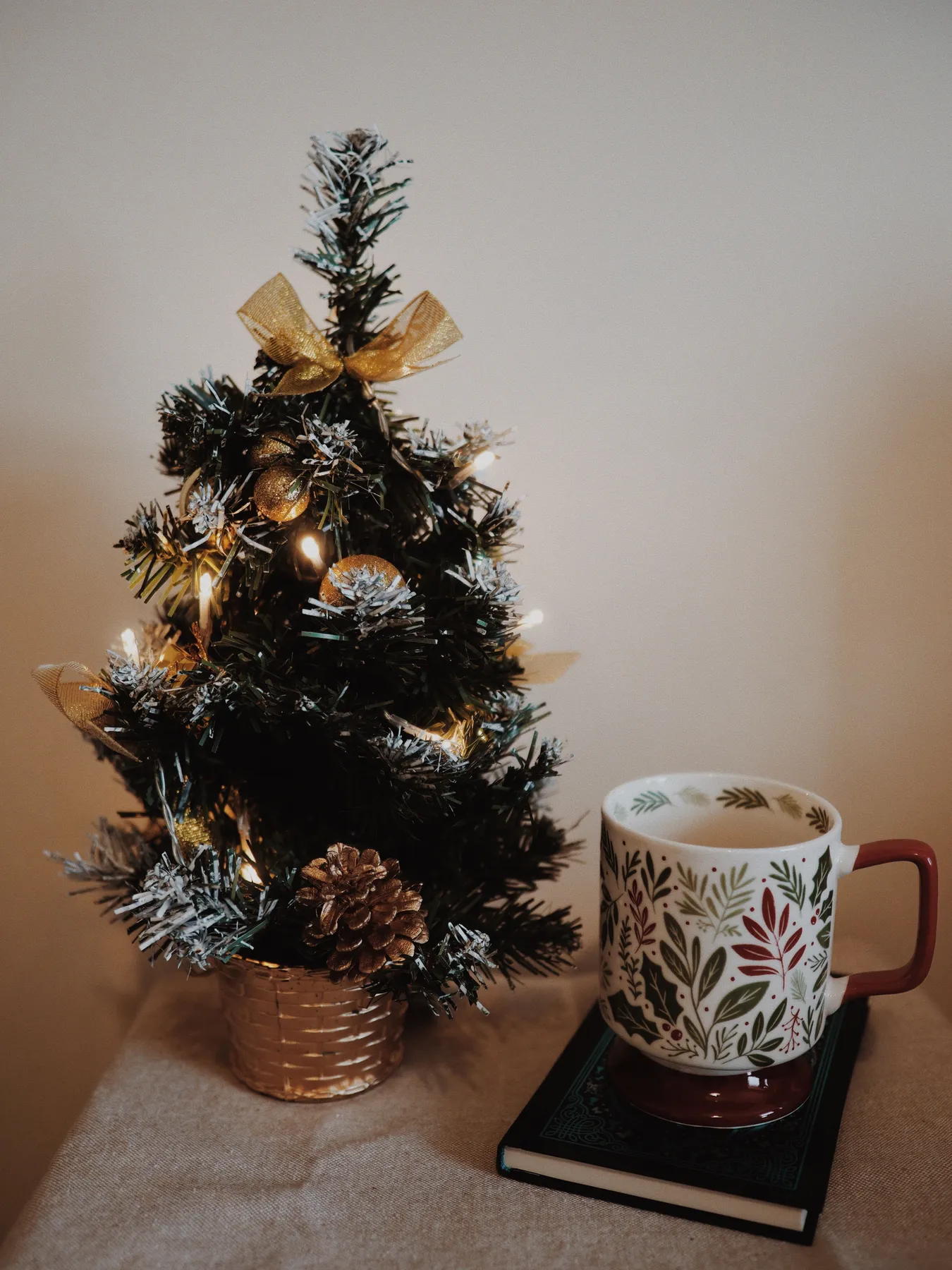 Charming mini Christmas tree with warm lights, mug, and book creating a cozy holiday feel.