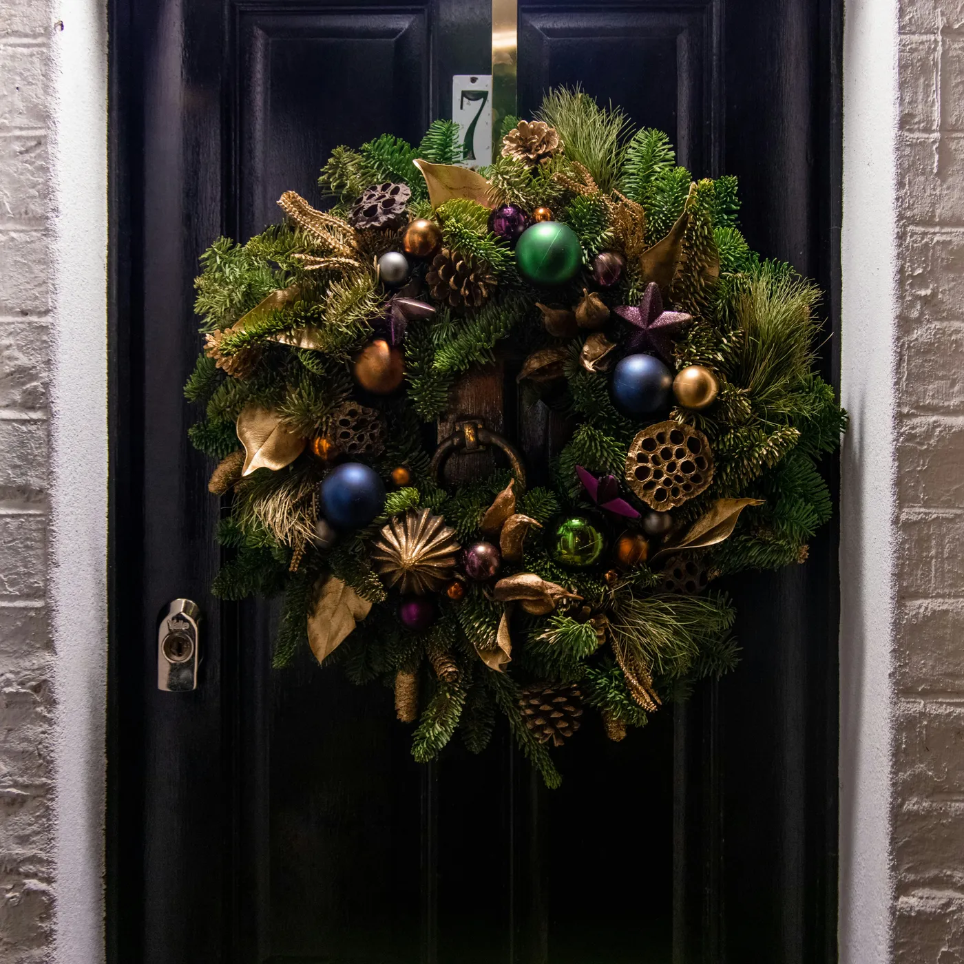 Christmas wreath on black door with green, purple, blue and gold accents. 