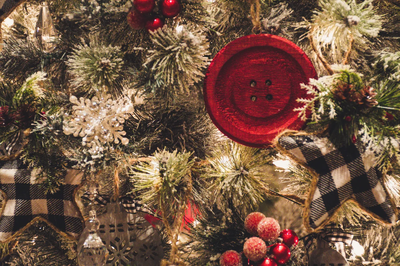 Close-up of a Christmas tree decorated with a red button, snowflakes, berries, and ornaments, creating a festive holiday atmosphere.