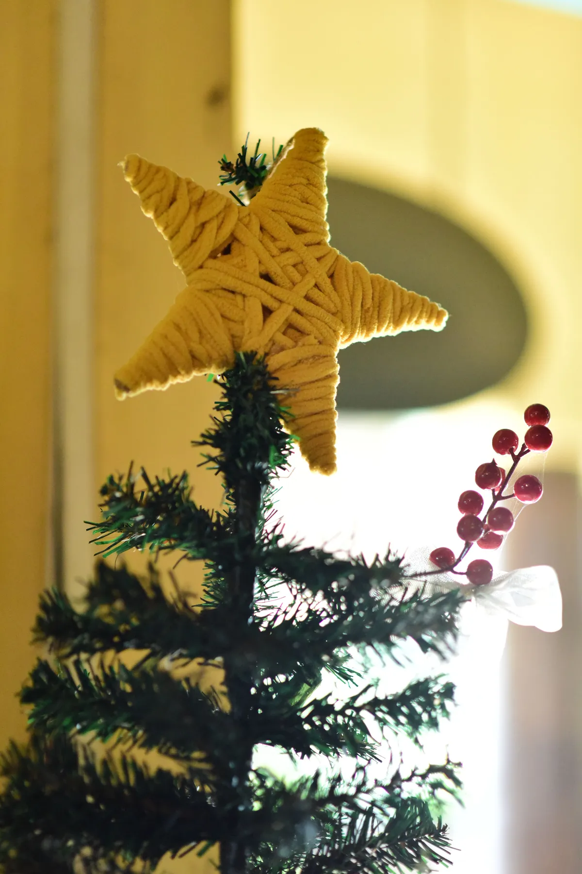 Close-up of a Christmas tree with a yarn star topper indoors capturing holiday spirit.