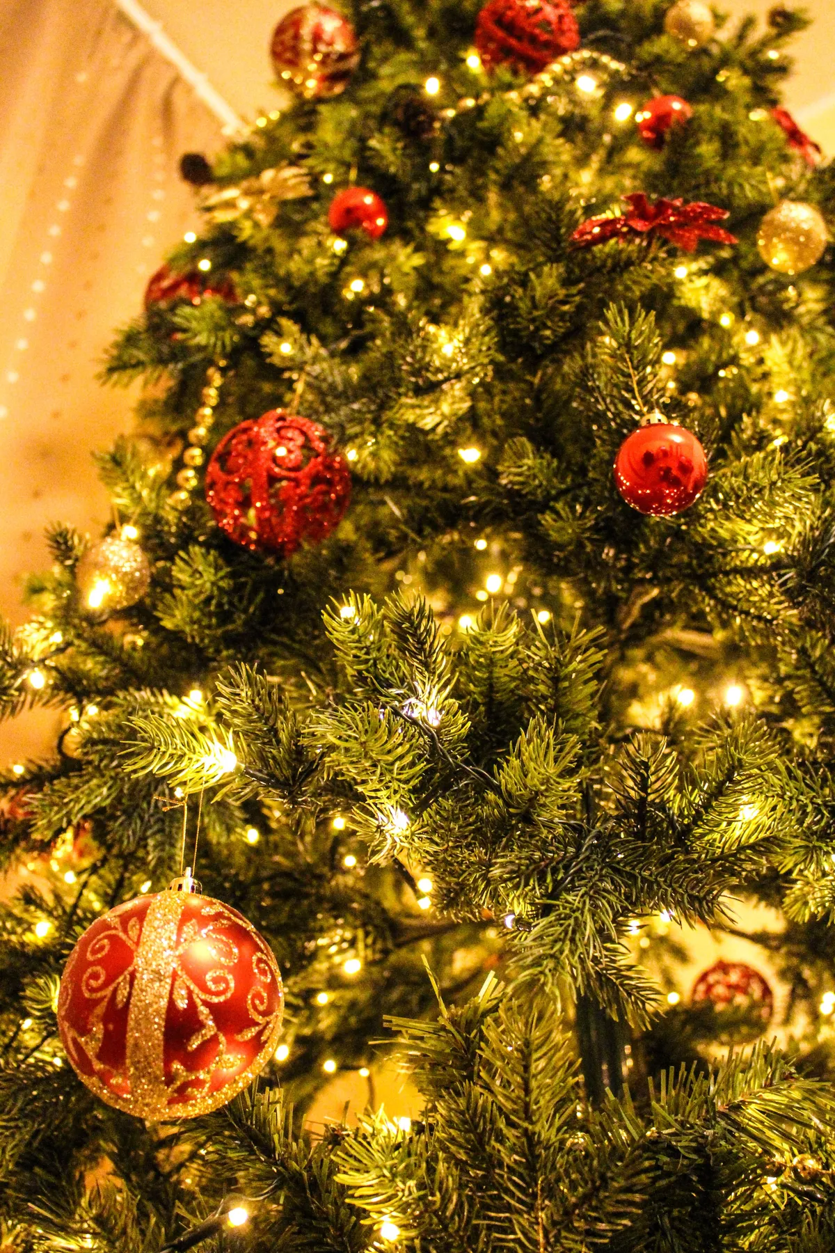 Close-up of a decorated Christmas tree featuring golden lights and red ornaments.