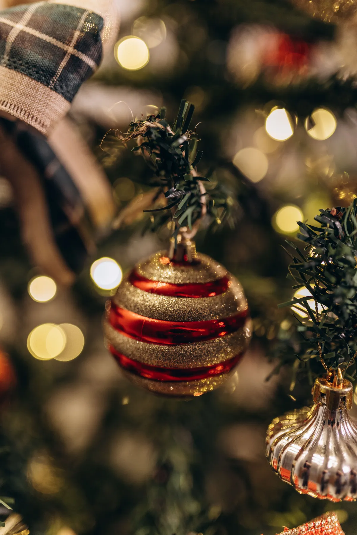 Close-up of a glittering red and gold bauble on a decorated Christmas tree.