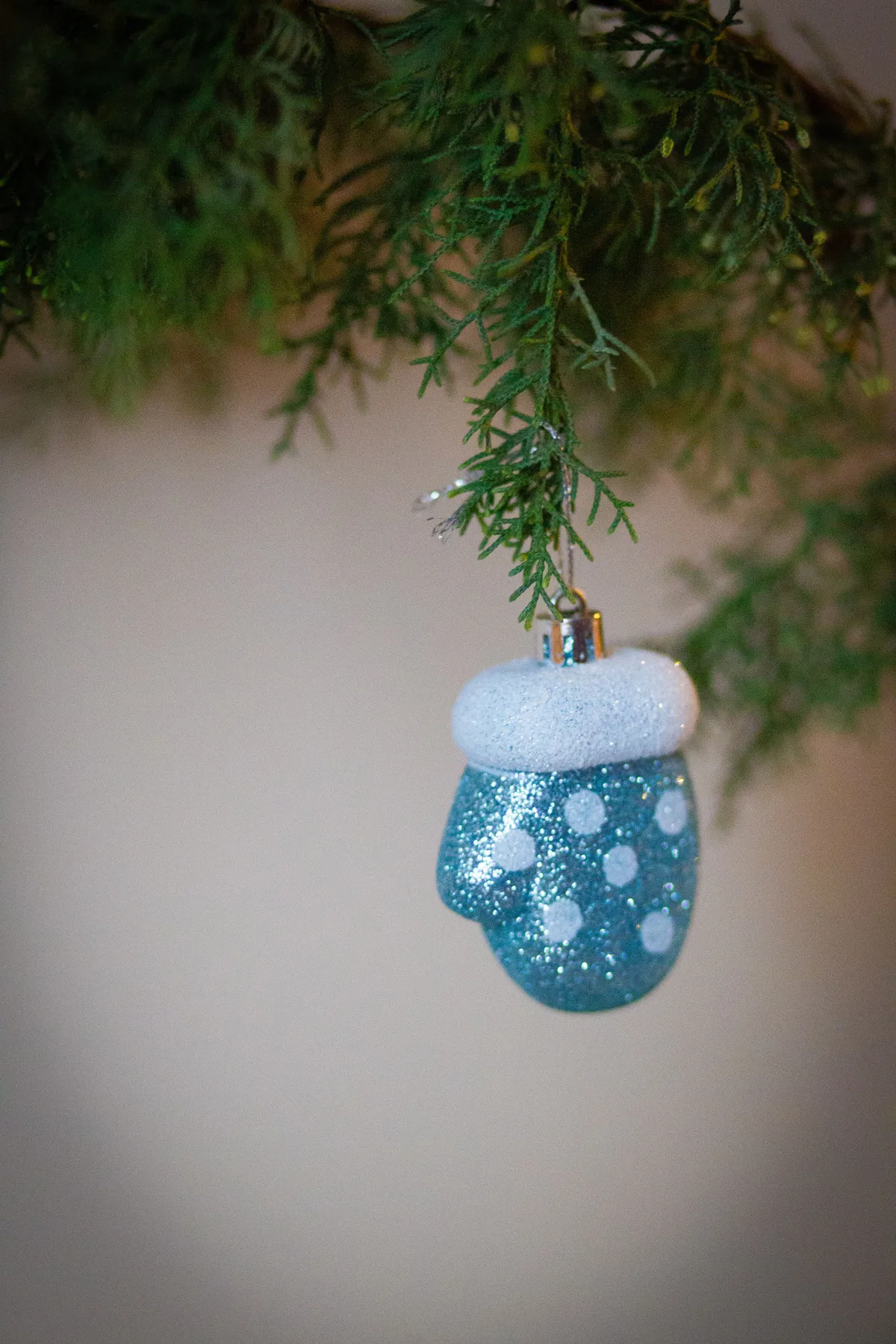 Close-up of a glittery blue mitten ornament hanging on a Christmas tree branch.