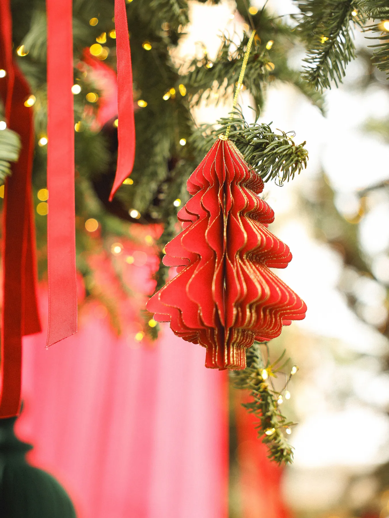 Close-up of a red Christmas tree ornament hanging on a decorated branch with lights.