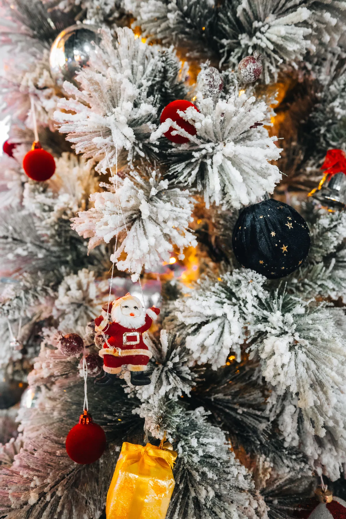 Close-up of a snow-covered Christmas tree adorned with vibrant ornaments and Santa figurine.