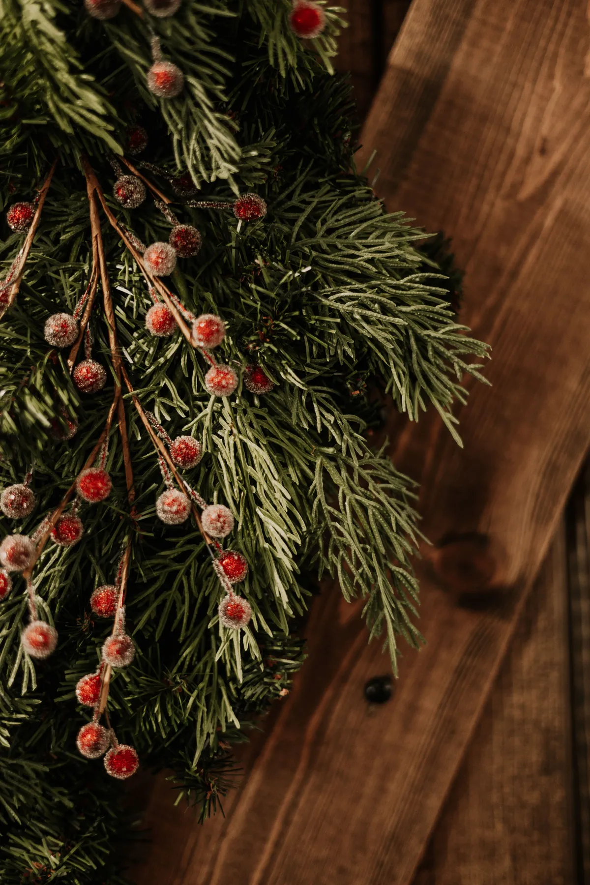 Close-up of evergreen branches with frosted red berries on a wooden background, perfect for Christmas or winter themes.