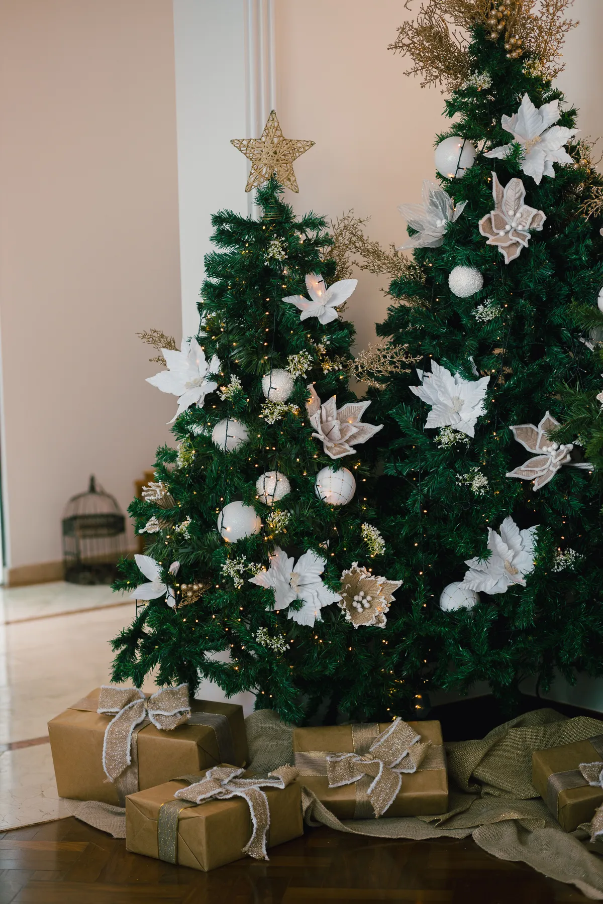 Decorated Christmas trees with golden and white ornaments and presents underneath in a bright room.