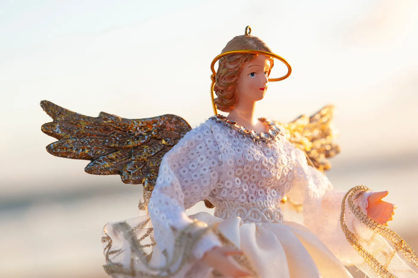 Decorative angel figurine with wings, halo, and lace dress captured in warm sunlight.
