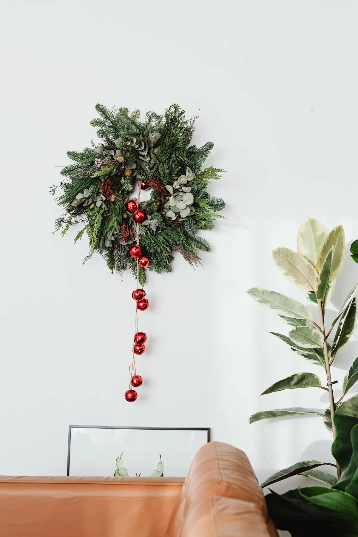 Elegant Christmas wreath with red ornaments on white wall in a stylish living room, enhancing holiday decor.