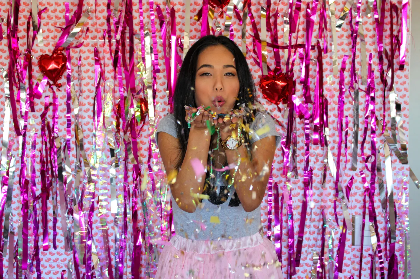 Festive celebration with a woman blowing confetti indoors with pink decorations.