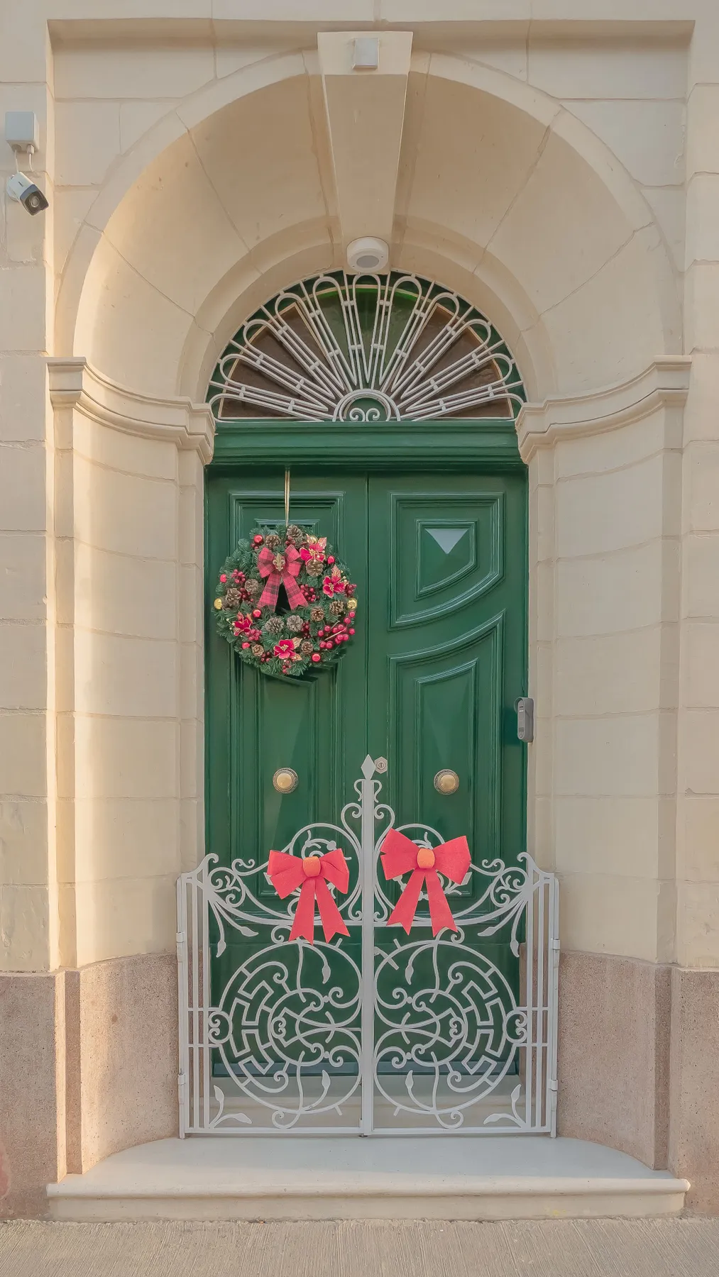 Festive green door adorned with a holiday wreath and red bows on a decorative gate.