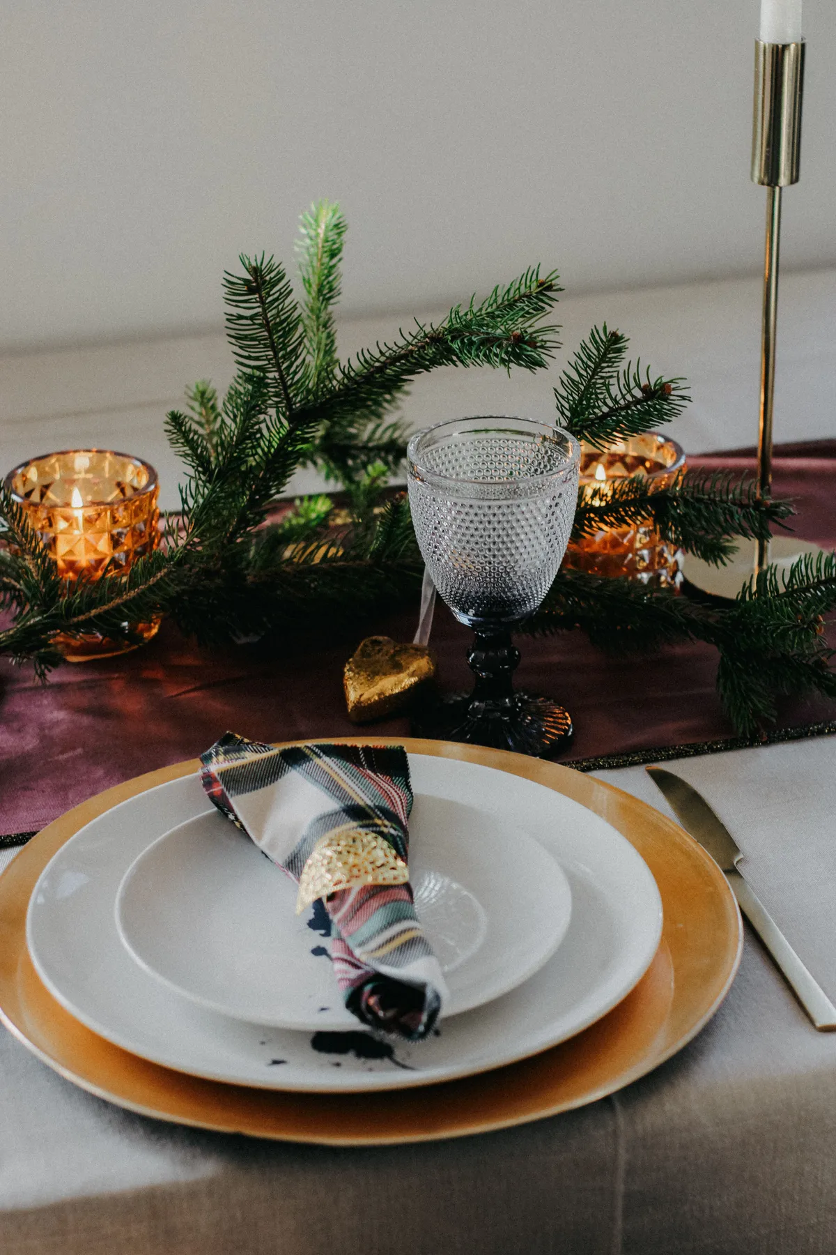 Festive holiday table setting with candles, pine branches, and elegant dinnerware.