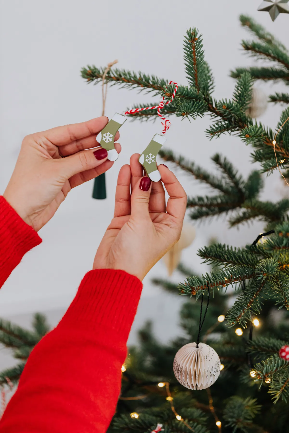 Hands placing ornaments on a Christmas tree, adding festive cheer.