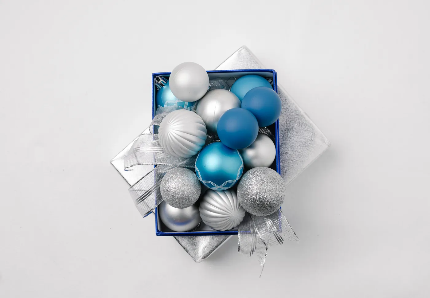 Top view of silver and blue balls placed on lid of gift box with ribbon on white background during Christmas holiday