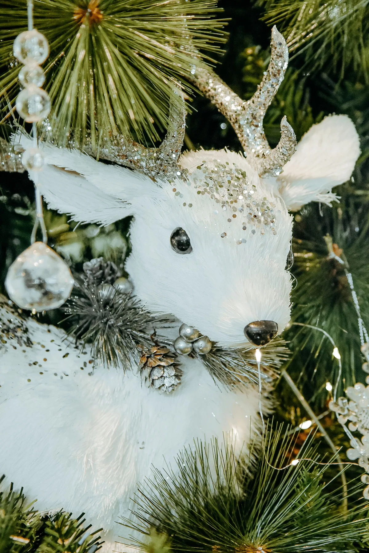 White reindeer ornament with glitter antlers on a decorated Christmas tree.